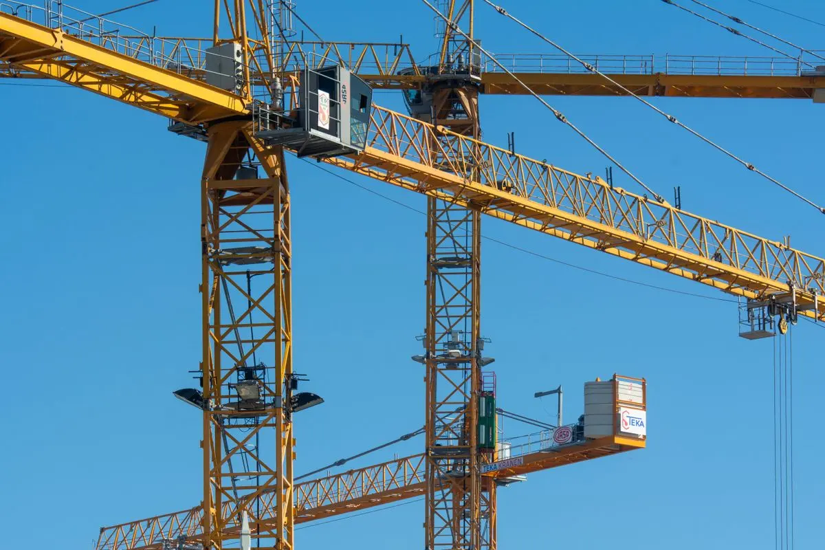 Illustrative photo: yellow tower cranes against a clear blue sky