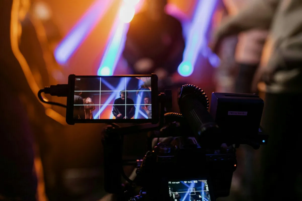 Camera monitor showing performers on a stage lit with blue and purple beams