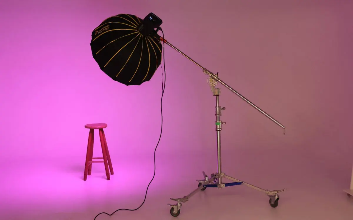 Illustrative photo: studio light on a boom stand beside a pink stool