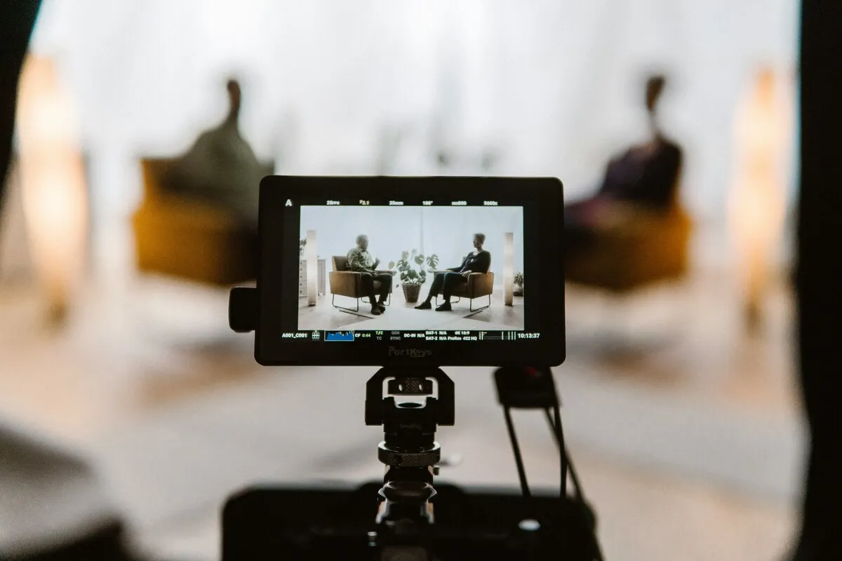 Camera monitor showing two people seated for an interview in a bright studio, with the real scene blurred behind