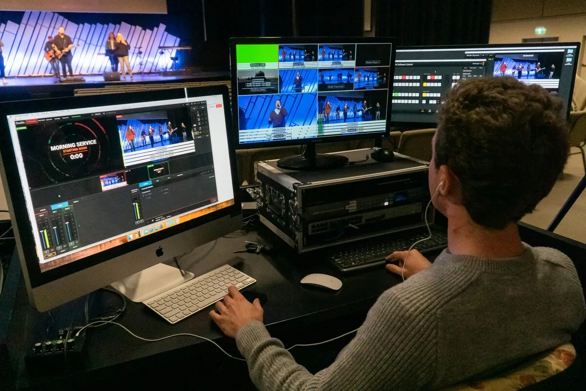 Vision mixer operator at a desk with several monitors showing live camera feeds of a stage performance